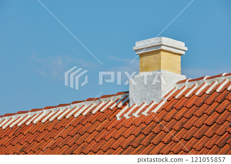 Brick chimney designed on slate roof of house building outside against blue sky background. Construction of exterior architecture of escape chute built on rooftop for fireplace smoke and heat 121055857
