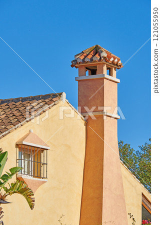 Chimney designed on roof of orange painted house building outside against blue sky background. Construction of exterior architecture of escape chute built on rooftop for fireplace smoke and heat 121055950