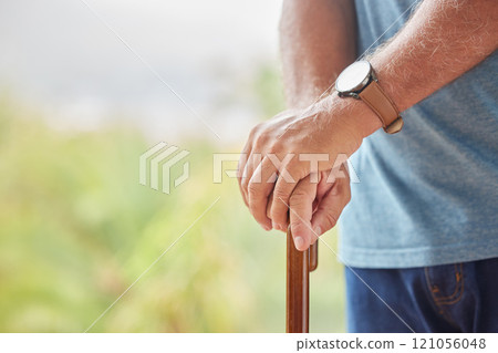 Senior disabled man hands holding a cane outside in a nursing home park. Closeup of elderly male holding a walking aid outdoors, relaxing at a healthcare facility on the sunny day 121056048