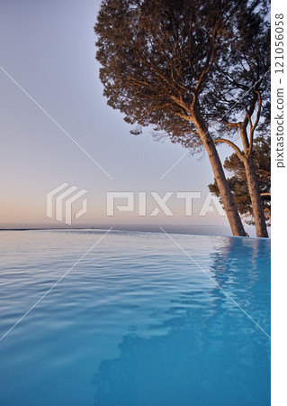 An infinity edge pool with trees against a blue sky background with copyspace. Beautiful outdoor swimming pool at a resort or luxury holiday villa against. Romantic getaway with a sea view in summer An infinity edge pool with trees against a blue sky background with copyspace. Beautiful outdoor swimming pool at a resort or luxury holiday villa against. Romantic getaway with a sea view in summer 121056058