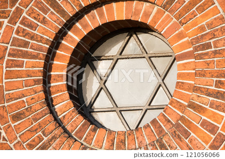View of a pentagram sign and symbol on an old round window on a red brick wall. Vintage glass with metal frame and pentagon on historic church building and background. Architecture circular design 121056066