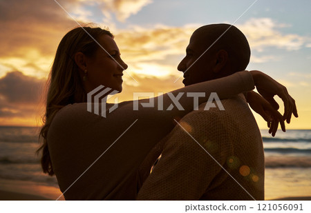 Loving young affectionate interracial couple in silhouette facing each other while spending time together on the beach at sunset. Lovers sharing romantic moment against golden sky while on vacation 121056091