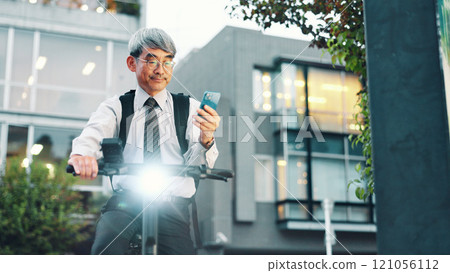 Businessman, mobile or electrical bike in city for travel, clean energy or sustainable transport. Commute ride, mature or eco friendly bicycle with phone or technology for location or map in Japan 121056112