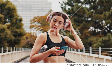 Fitness, woman and headphones with phone in city of listening to music, cardio podcast and social media. Athlete, mobile app and streaming radio of exercise routine, training website and Japan bridge Fitness, woman and headphones with phone in city of listening to music, cardio podcast and social media. Athlete, mobile app and streaming radio of exercise routine, training website and Japan bridge 121056272