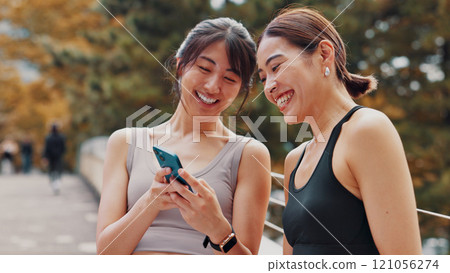Japan, exercise and women with cellphone, fitness and typing with funny meme. Laughing, outdoor and runners with smartphone, happiness and tech for online reading, digital app and workout with humor 121056274