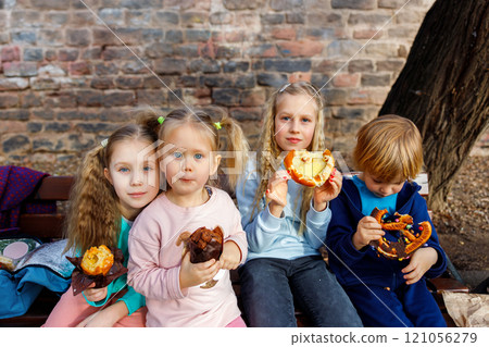 Portrait group happy funny playful blond children enjoy eating pretzels chocolate toppings at city street outdoor park. Scenic fun moment capturing kids childhood joy snacking on colorful treats Portrait group happy funny playful blond children enjoy eating pretzels chocolate toppings at city street outdoor park. Scenic fun moment capturing kids childhood joy snacking on colorful treats 121056279