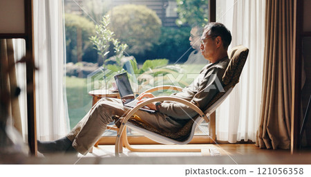 Laptop, relax and mature with Japanese man at home for blog writer, online research and article. Social media, internet and freelancer with person in living room for connection, remote work and email 121056358