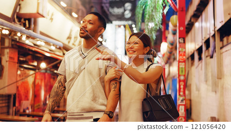 Couple, night and outdoor market for walking in Japan, love and bonding on honeymoon vacation. People, pointing and support on holiday in town, travel together and explore culture or sightseeing Couple, night and outdoor market for walking in Japan, love and bonding on honeymoon vacation. People, pointing and support on holiday in town, travel together and explore culture or sightseeing 121056420
