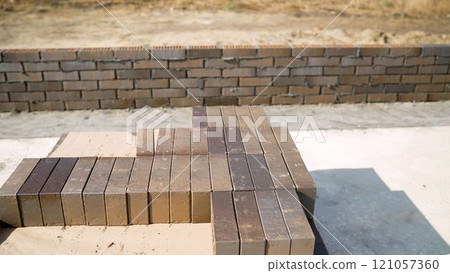 Brown bricks on a construction site, building a private house. Concept of building a house from bricks. New bricks on a house construction. Bricks stacked in a row, ready for transportation, brick Brown bricks on a construction site, building a private house. Concept of building a house from bricks. New bricks on a house construction. Bricks stacked in a row, ready for transportation, brick 121057360