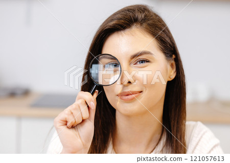 A cute young girl is holding a magnifying glass and looking at the camera A cute young girl is holding a magnifying glass and looking at the camera 121057613