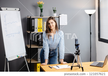 Young woman mentor recording presentation, webinar on smartphone standing on tripod, teacher coach explaining, holding online lesson, using phone webcam. 121057621