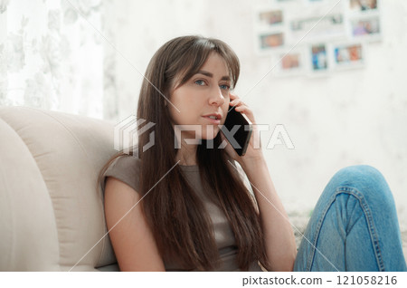 Relaxed young woman chatting on the phone while lounging on a couch in her living room 121058216
