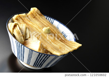 Conger eel rice bowl topped with wasabi and pickled ginger photographed against a black background 121058602