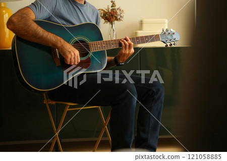 Close-up of a man's hands playing a chord with his fingers on acoustic guitar at home 121058885