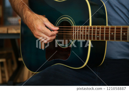 Close-up of a man's hands playing a chord with his fingers on acoustic guitar at home 121058887