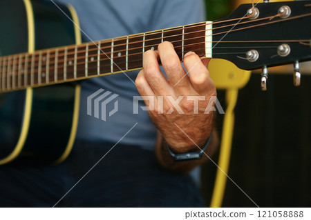 Close-up of a man's hands playing an D chord on acoustic guitar at home Close-up of a man's hands playing an D chord on acoustic guitar at home 121058888