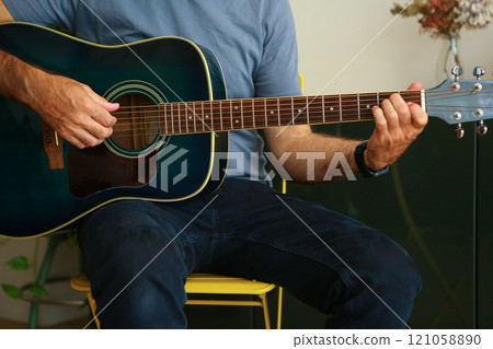 Close-up of a man's hands playing an E chord on acoustic guitar at home Close-up of a man's hands playing an E chord on acoustic guitar at home 121058890