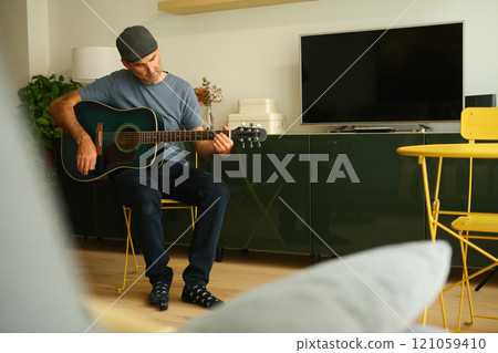 A man sitting at home learning to play a chord on acoustic guitar A man sitting at home learning to play a chord on acoustic guitar 121059410