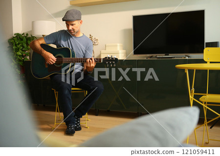 A man sitting at home learning to play a chord on acoustic guitar 121059411
