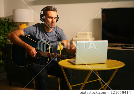 A man sitting in front of the computer practicing online music lessons 121059414