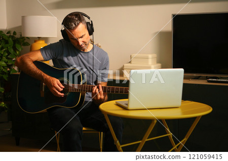 A man sitting in front of the computer practicing online music lessons A man sitting in front of the computer practicing online music lessons 121059415