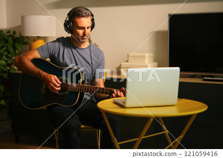 A man sitting in front of the computer practicing online music lessons 121059416