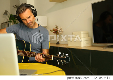 A man sitting in front of the computer practicing online music lessons A man sitting in front of the computer practicing online music lessons 121059417