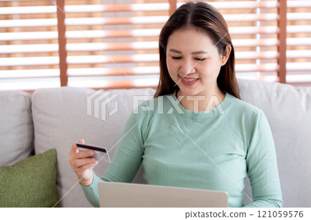 Young asian woman sitting on sofa using laptop computer shopping online with credit card buying. Young asian woman sitting on sofa using laptop computer shopping online with credit card buying. 121059576