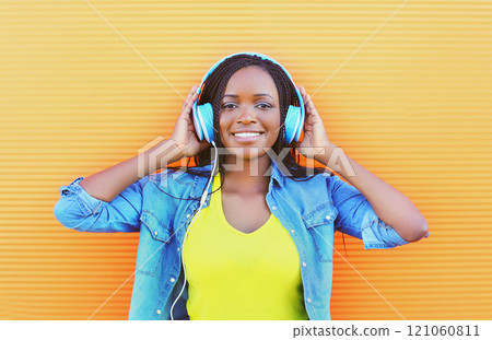 Beautiful smiling african woman with headphones enjoying listens to music over orange background 121060811