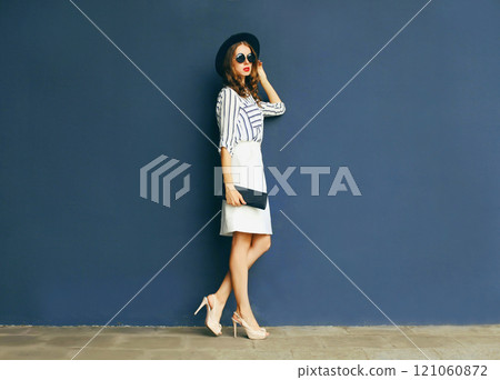 Fashion elegant woman in a black hat and white skirt with a handbag clutch over a gray background Fashion elegant woman in a black hat and white skirt with a handbag clutch over a gray background 121060872