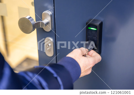 Close up view of person using a electric lock key fob to access a building via a reader of entry system mounted on a house wall 121061001