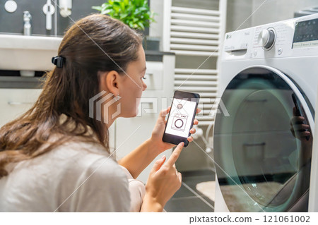 Young woman using mobile phone control via wi-fi and app for washing machine in home. Homesmart and new technology concept Young woman using mobile phone control via wi-fi and app for washing machine in home. Homesmart and new technology concept 121061002