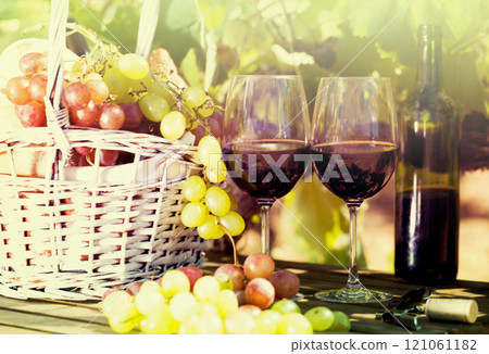 Still life with glass of red wine grapes and picnic basket on table 121061182
