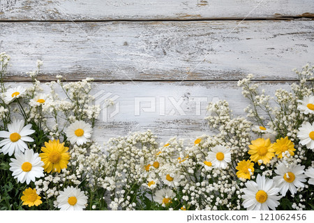 A old wooden plank background with a variety of yellow and white flowers, including daisies on the sides.  121062456