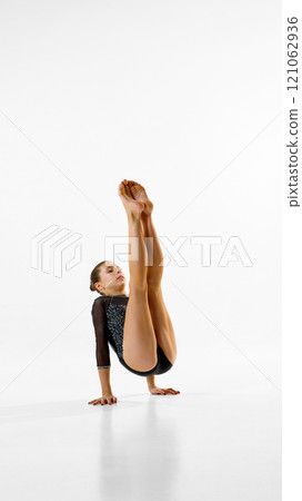 Female gymnast, artistic sportsman maintains strong focus, improving flexibility and control against white studio background. Copy space. 121062936