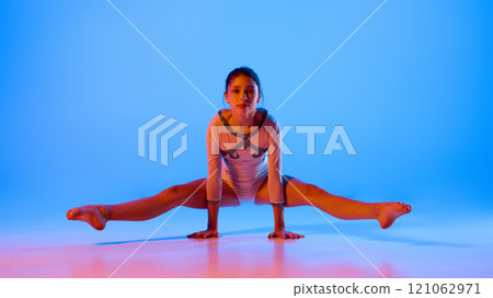 Gymnast practicing control and flexibility in pink neon light against gradient blue background. Gymnast practicing control and flexibility in pink neon light against gradient blue background. 121062971