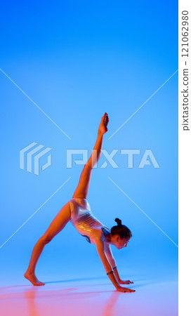 Young athlete demonstrates incredible control and flexibility, showcasing dedication during intense training in pink neon light against gradient blue background. 121062980