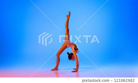 Showcasing strength and poise, gymnast performs flawless handstand, in pink neon light against gradient blue background. 121062982