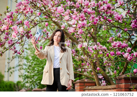 Woman taking selfie with smartphone among spring blossoms with soft focus on the background. Woman taking selfie with smartphone among spring blossoms with soft focus on the background. 121063752