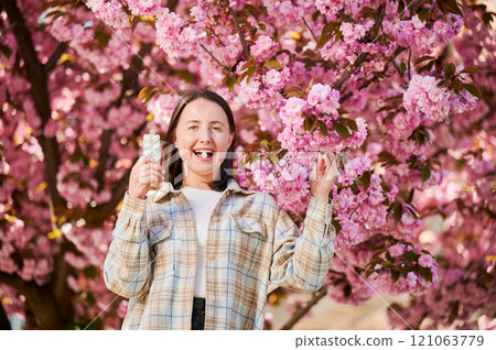Woman allergic suffering from seasonal allergy at spring. Young happy woman applying allergy drug, posing in blossoming garden at springtime. Antihistamine medication concept 121063779