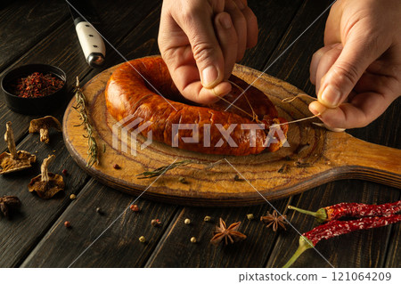 A skilled artisan carefully ties fresh sausage on a handcrafted wooden board. Surrounding ingredients include vibrant spices and herbs, creating an inviting culinary atmosphere A skilled artisan carefully ties fresh sausage on a handcrafted wooden board. Surrounding ingredients include vibrant spices and herbs, creating an inviting culinary atmosphere 121064209