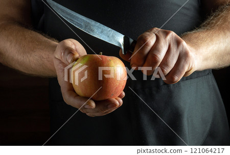 A pair of hands hold a vibrant apple while a knife hovers above it, poised for cutting. Soft light filters into the kitchen, creating a warm and inviting atmosphere for culinary creativity A pair of hands hold a vibrant apple while a knife hovers above it, poised for cutting. Soft light filters into the kitchen, creating a warm and inviting atmosphere for culinary creativity 121064217
