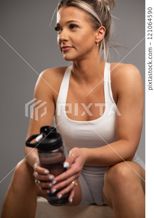 Young active woman sitting with water bottle during a workout break 121064590