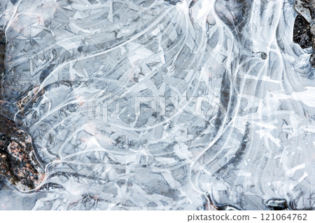 Abstract pattern of thin ice is on frozen puddle, natural background 121064762