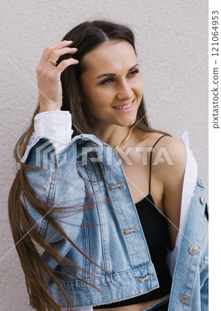 Smiling young woman wearing a blue jacket and black tank top is smiling. She has long hair and is wearing a ring on her left hand Smiling young woman wearing a blue jacket and black tank top is smiling. She has long hair and is wearing a ring on her left hand 121064953