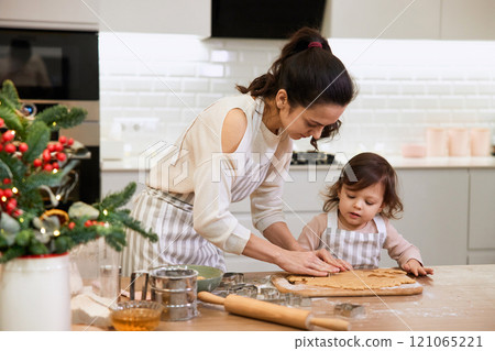 Happy family mother and little child daughter cutting cookies of raw gingerbread dough in kitchen. Christmas time 121065221
