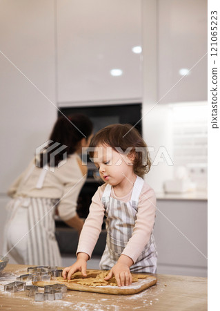 Cute little child girl in apron helping mom bake cookies in the kitchen Cute little child girl in apron helping mom bake cookies in the kitchen 121065223