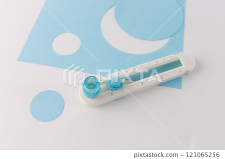 Paper circle cutter tool with blue cutouts on a white background. Close-up. Arts and crafts tool concept for design and print. manual rotary trimmer for DIY, craft and precise cut out , top view 121065256