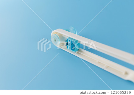 a close-up view of a plastic circle cutter device with a small blade cutting tool. a crafting or DIY context. soft focus, upside down view, blue background, rotary manual cutter, 121065259