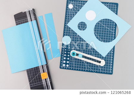 a collection of crafting tools and materials used for cutting circles. There is a blue cutting mat with a grid and various measurement markings, circular cutouts, and a paper trimmer tool, top view, 121065268